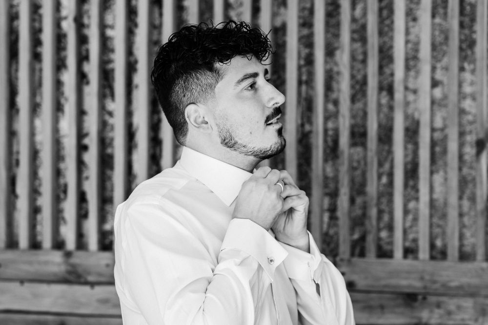 A person adjusts their bow tie while standing against a wooden fence background.