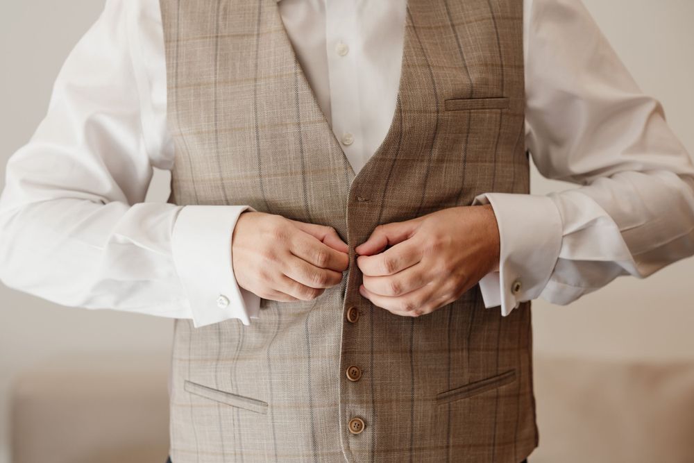 Hands buttoning up a textured beige vest over a crisp white shirt.