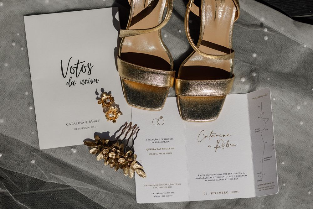 Wedding invitation suite with gold metallic heels and decorative elements on gray surface.