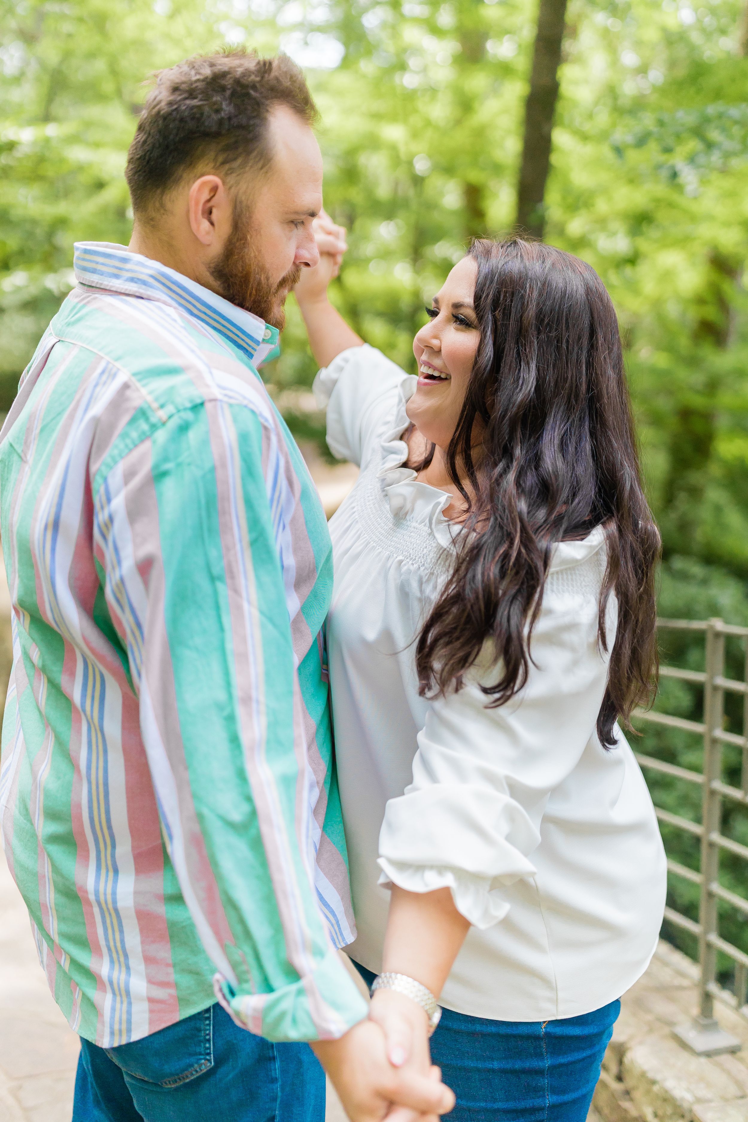 A couple sharing a playful moment on a wooden bridge surrounded by green forest.