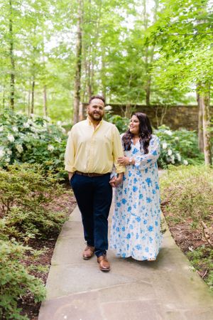 A couple walking along a garden path surrounded by lush greenery and hydrangeas.