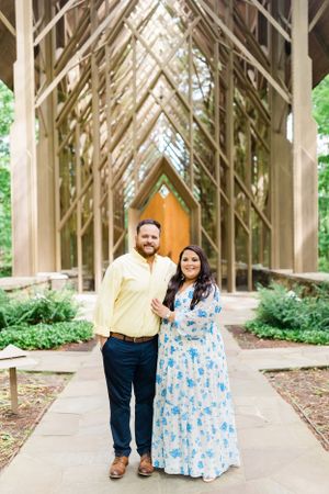 A couple stands together under a dramatic wooden archway in a garden setting with natural light.