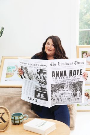 Woman holding Anna Kate Photography newspaper-style brochure while sitting in a bright photography studio office.
