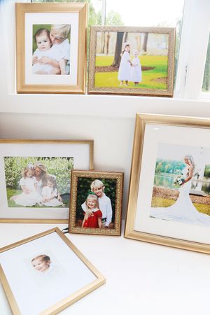 Collection of gold-framed family photos displayed on a white surface, including portraits, a wedding photo, and children pictures.