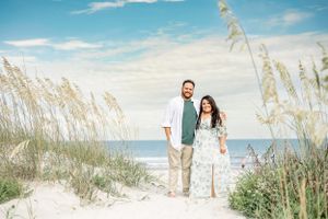A couple standing among beach sea oats with ocean and blue sky in the background.