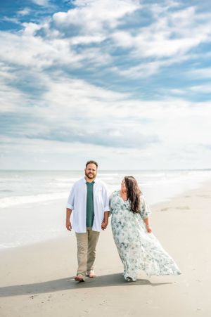 A couple walking along a pristine beach with cloudy blue skies overhead.