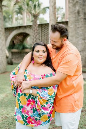 A couple embracing in a tropical garden setting with palm trees and stone architecture.