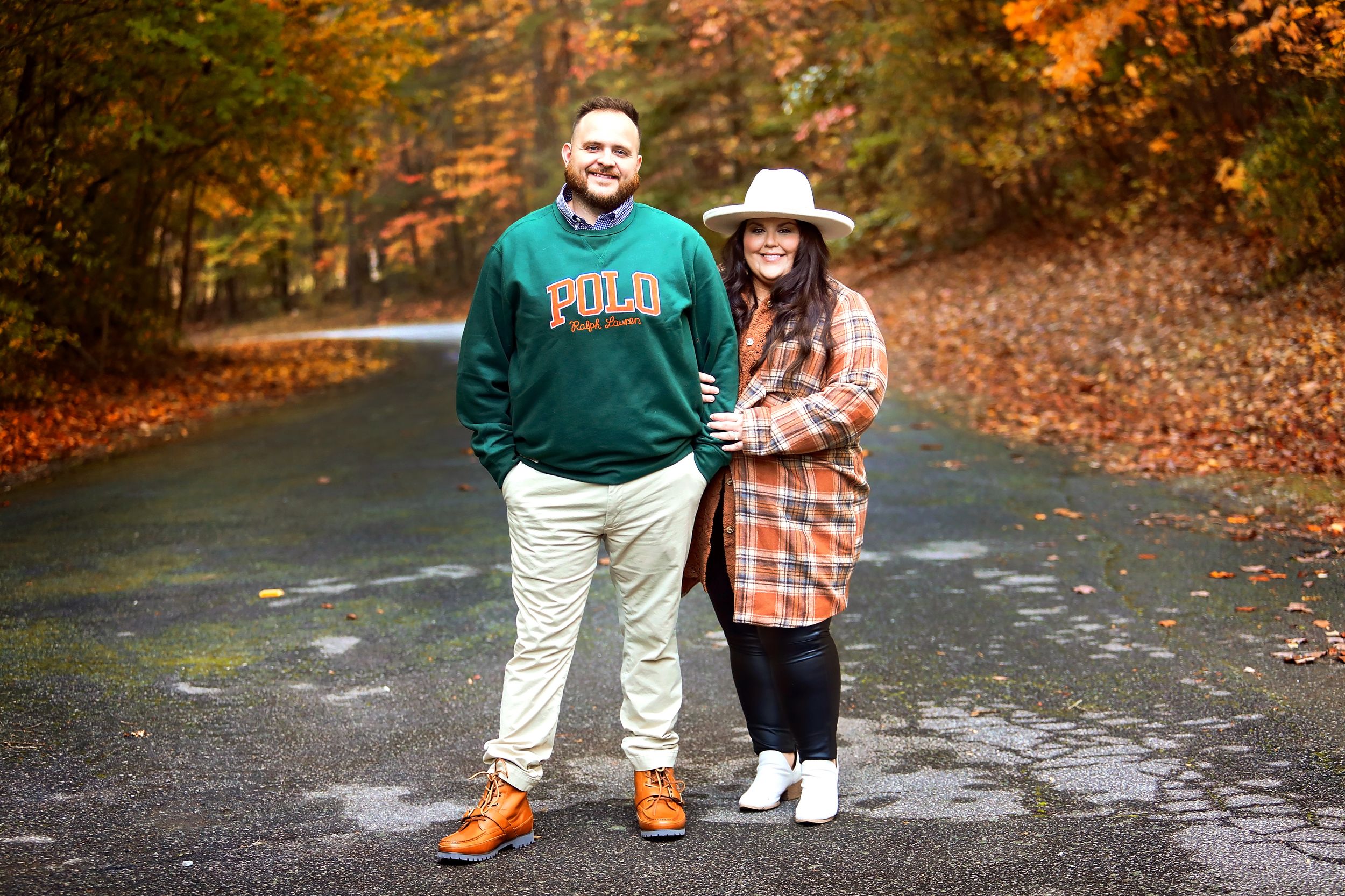 A couple posing on a leaf-covered path during autumn with fall foliage in the background.