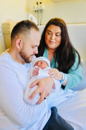 A newborn baby being cradled by parents in a hospital room setting.
