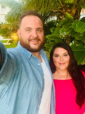 A couple taking a selfie outdoors with tropical foliage in the background.