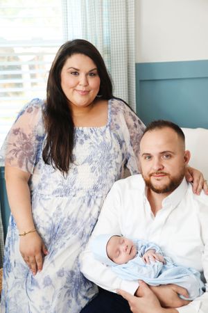 Family portrait in hospital room with newborn baby in blue outfit.