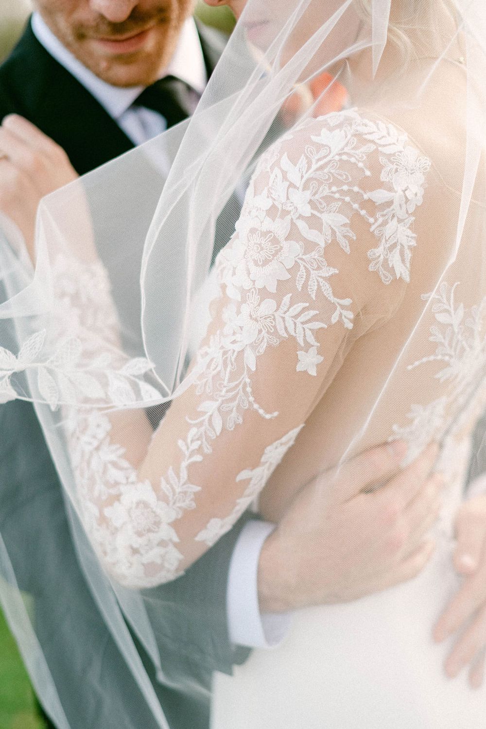Close-up detail of delicate white lace sleeves on a wedding dress with intricate floral embroidery patterns.