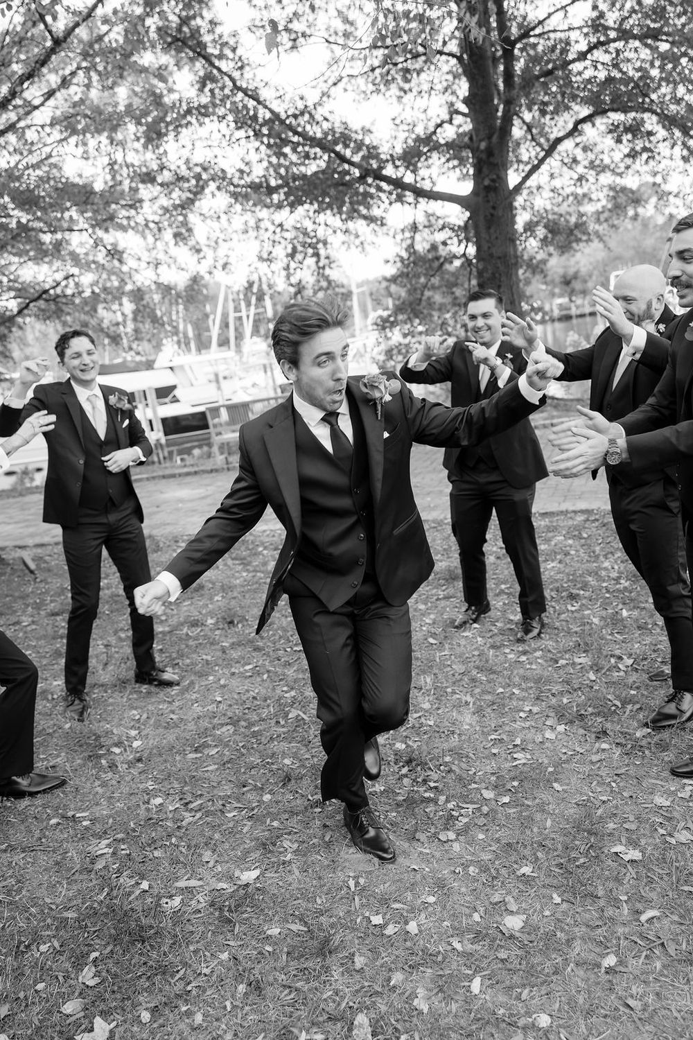 Groomsmen in black suits strike playful poses on grass in a candid black and white photo sequence.