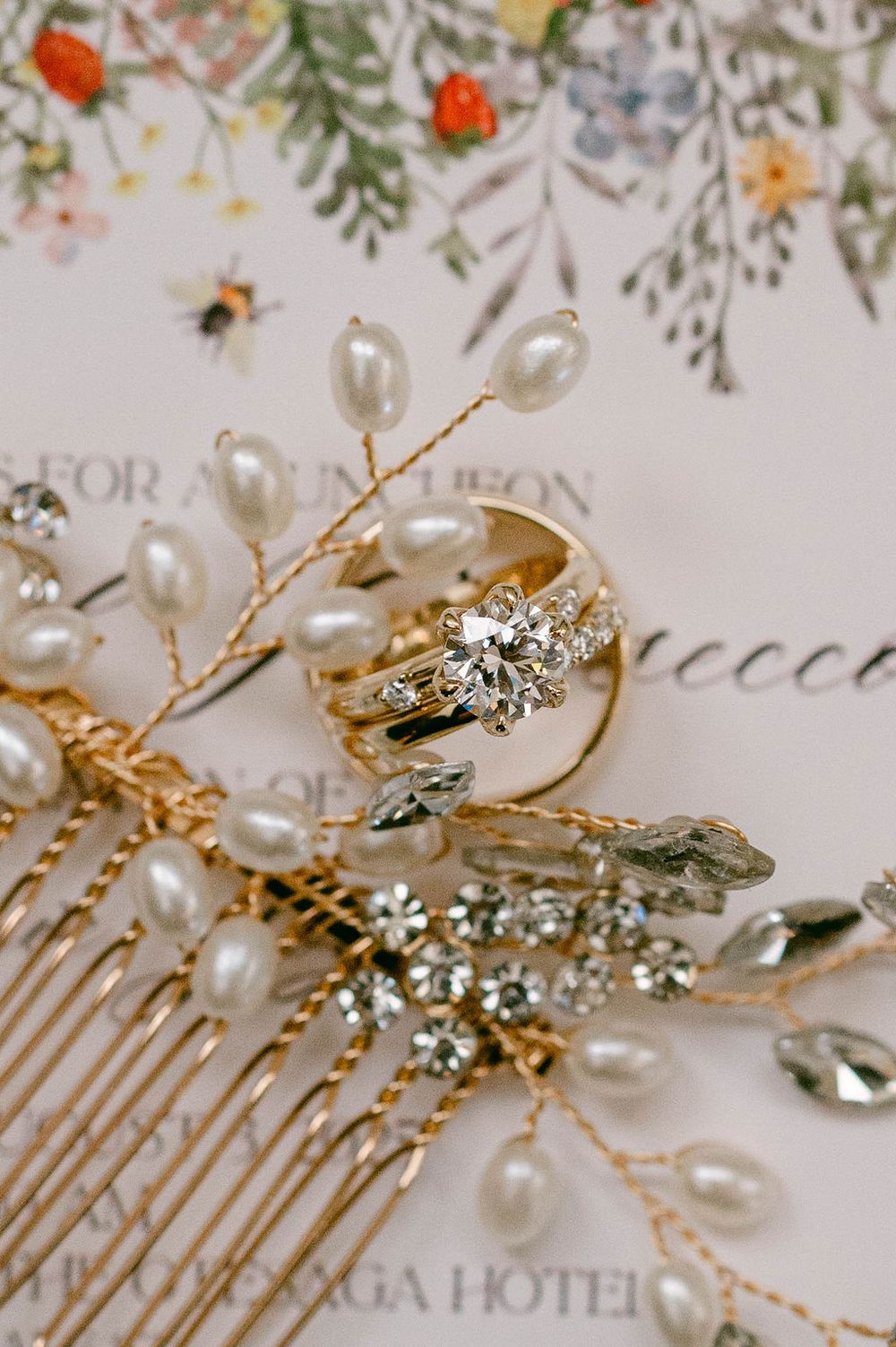 Ornate pearl and crystal wedding hair comb with floral design against invitation paper.