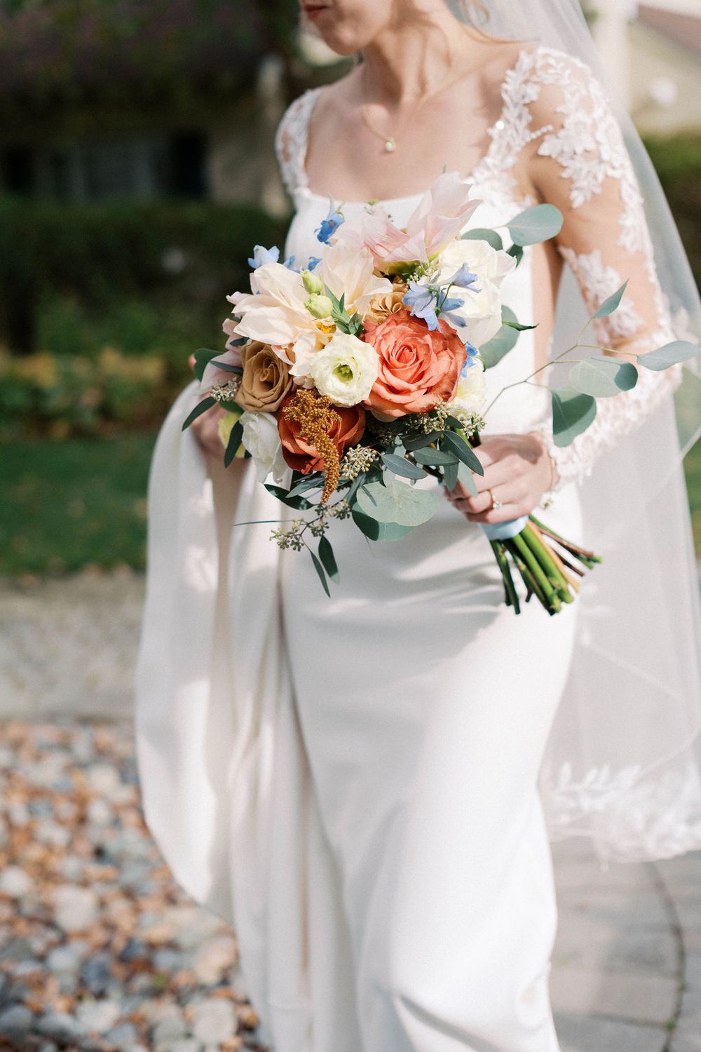 Close-up view of wedding bouquets with coral and peach roses, eucalyptus greenery, and delicate white lace details.