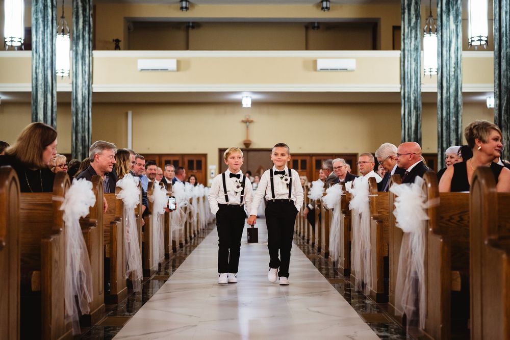 Wedding guests stand in a church aisle during a traditional ceremony with white pew decorations.