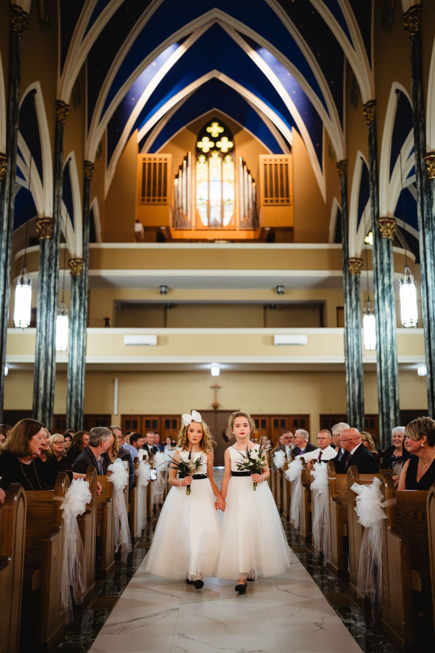 A church sanctuary with vaulted ceilings and blue-accented arches is set up for a wedding ceremony with decorated pews.