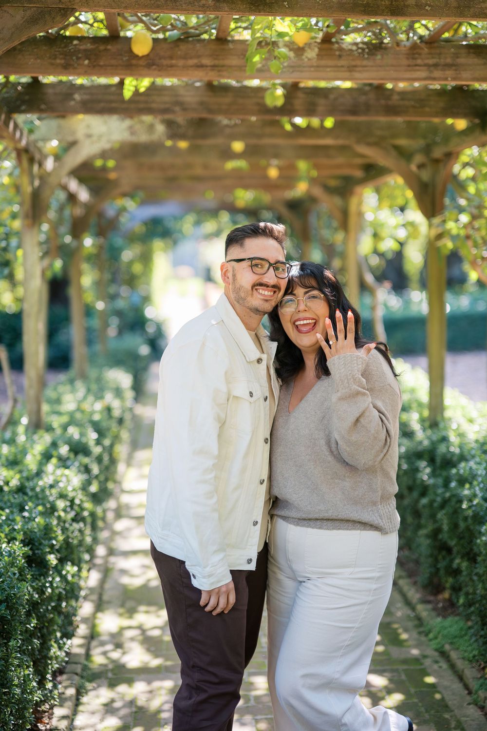 A couple shares joyful moments together under a vine-covered pergola in a garden setting.