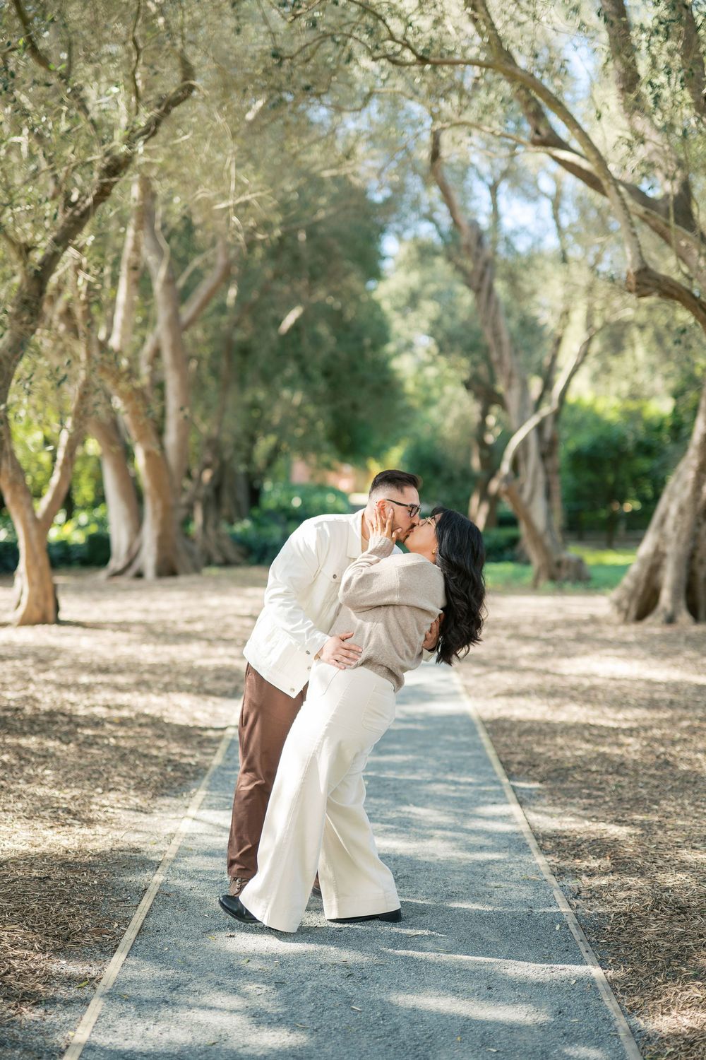 A couple shares an intimate moment on a tree-lined path in a romantic outdoor setting.