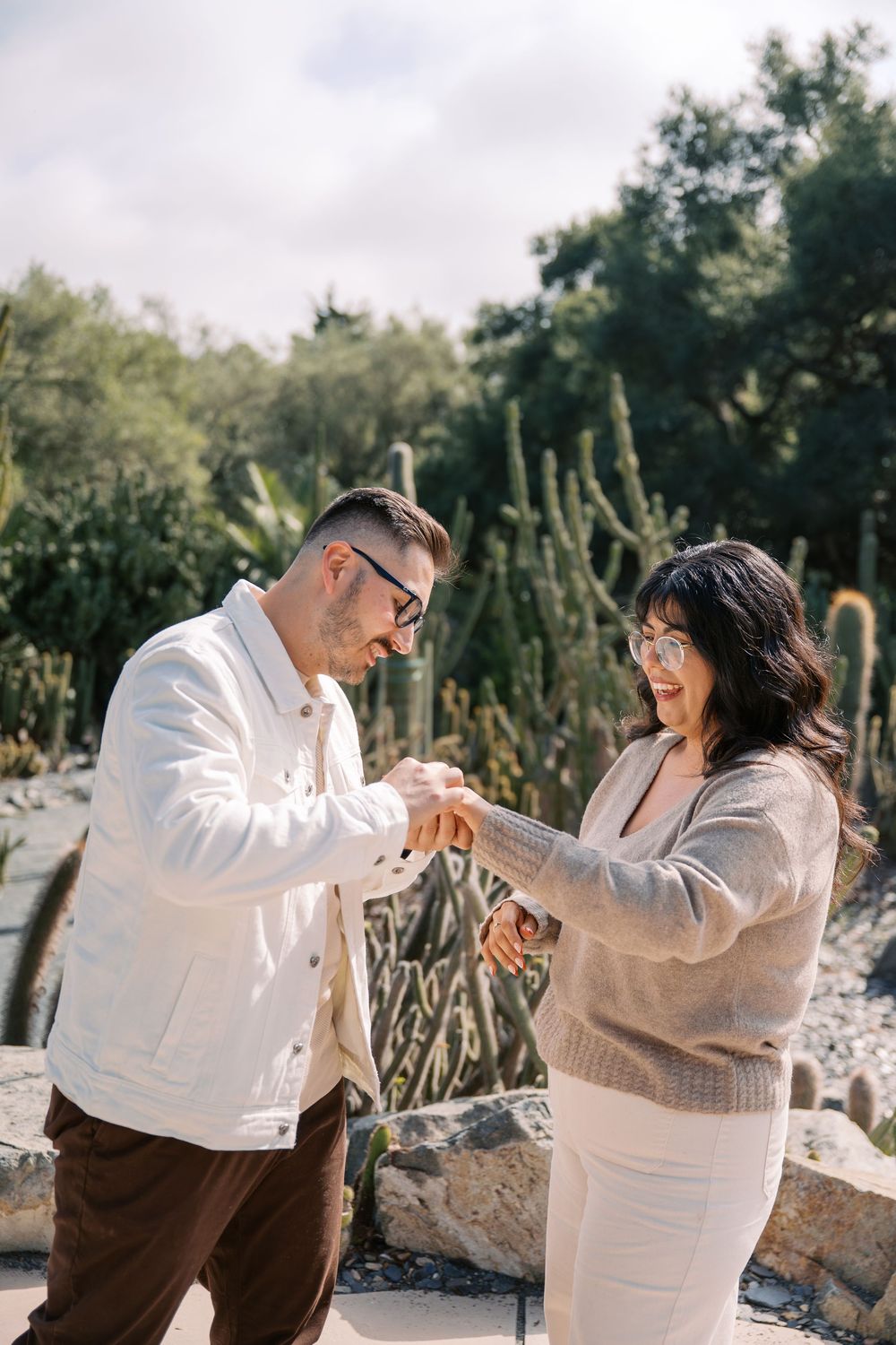 A playful couple in coordinated outfits dances and spins together in a natural outdoor setting.