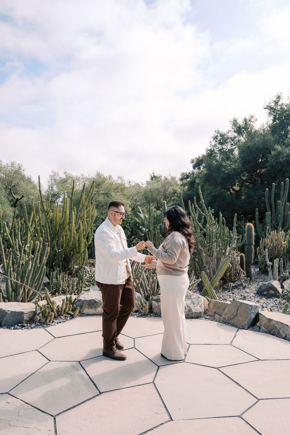 A couple poses on a geometric paved patio surrounded by desert cacti and succulents.