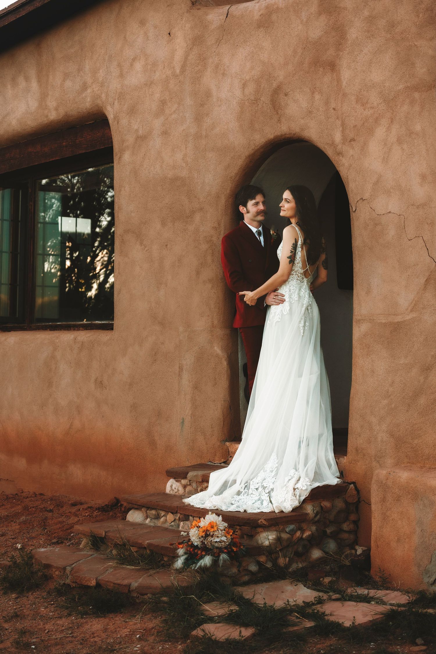 Bride and groom share a romantic moment in an arched doorway of a rustic adobe building at golden hour.