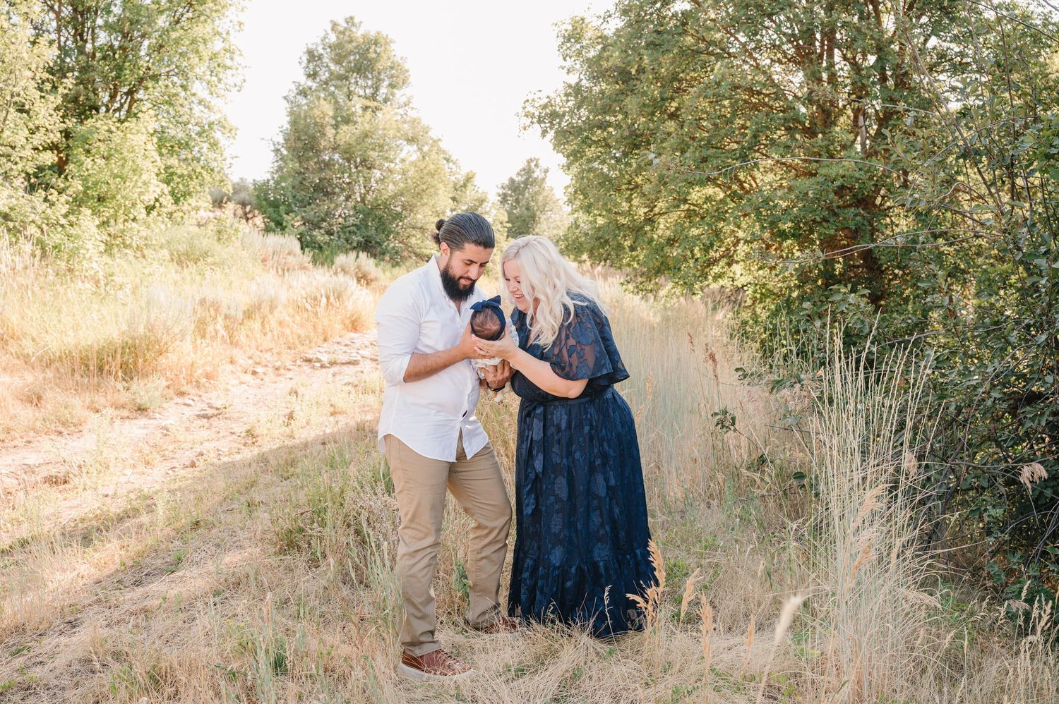 A couple poses together in a natural outdoor setting with trees and sunlight creating a romantic atmosphere.