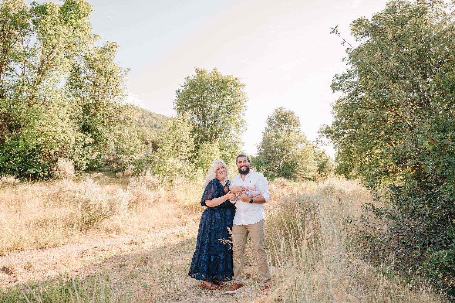 Romantic outdoor photoshoot with couples embracing among natural foliage and golden sunlight.