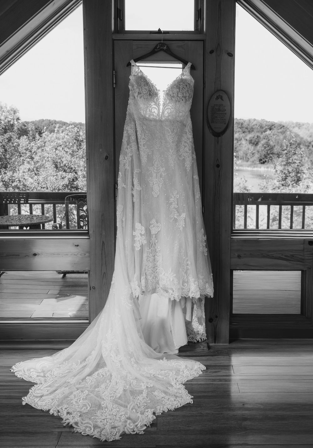 Elegant lace wedding dress hanging in a rustic wooden chapel window with a flowing train.