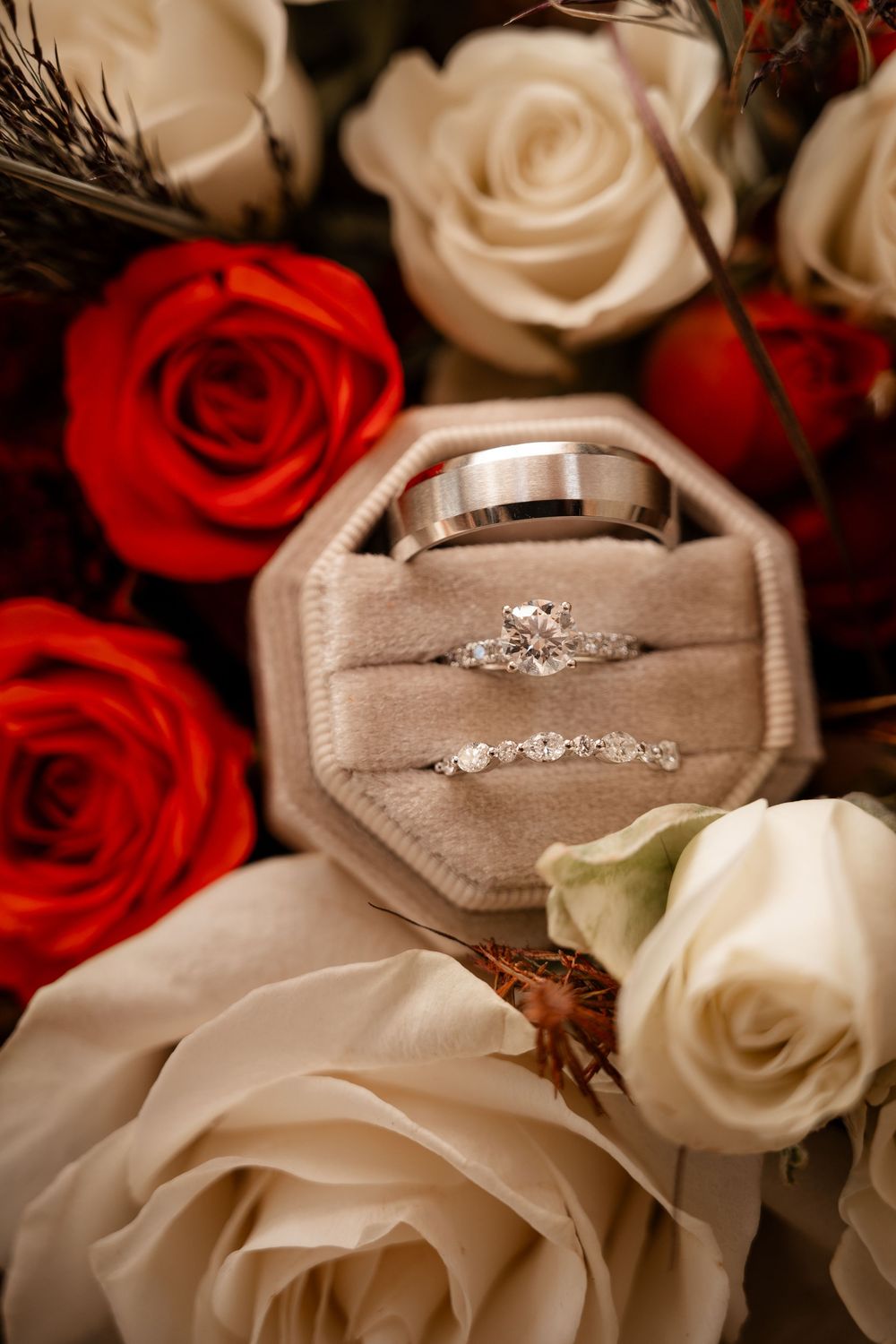 Diamond engagement ring and wedding bands displayed in velvet box surrounded by red and white roses.
