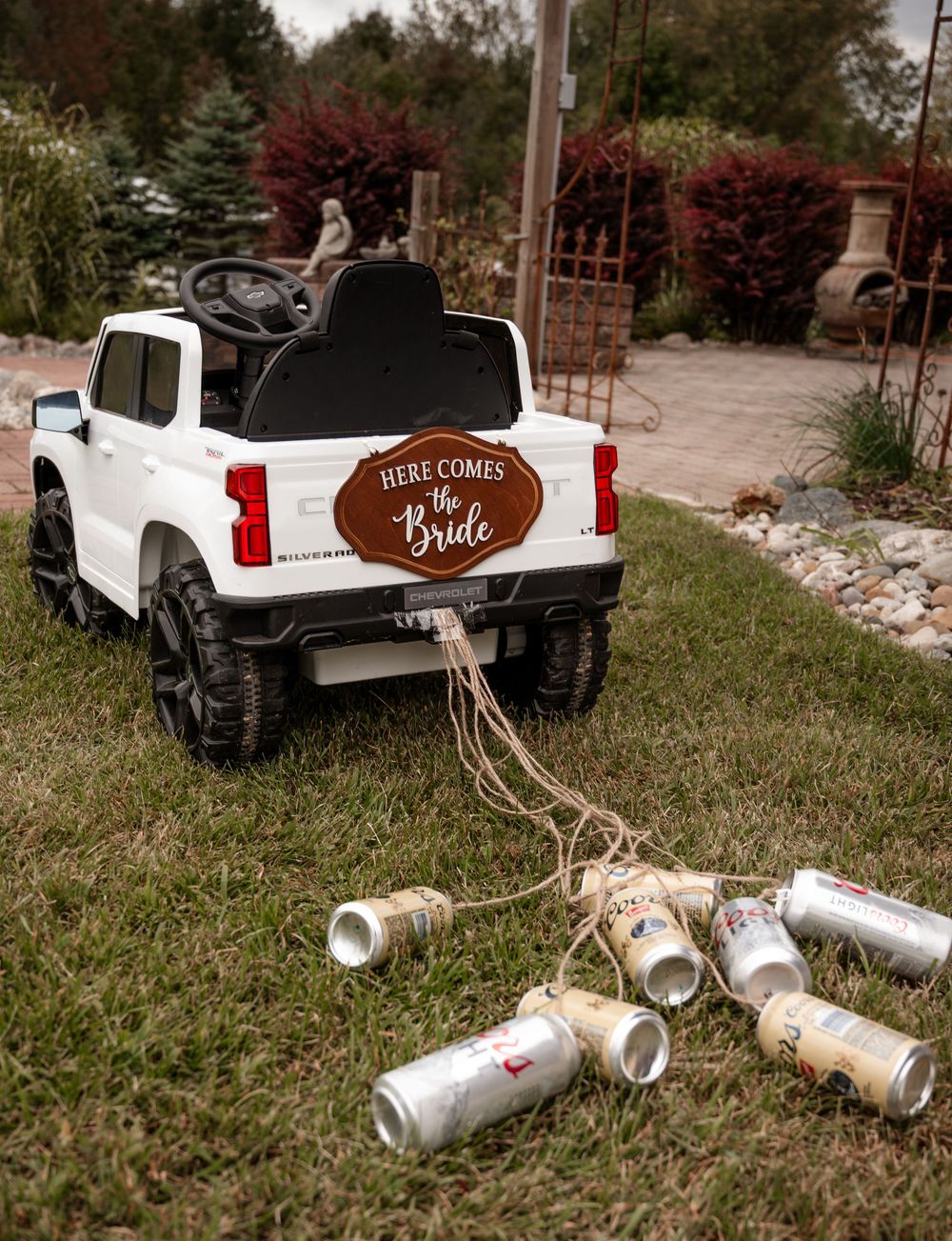 Toy pickup truck with Here Comes the Bride sign and tin cans tied to it on grass.
