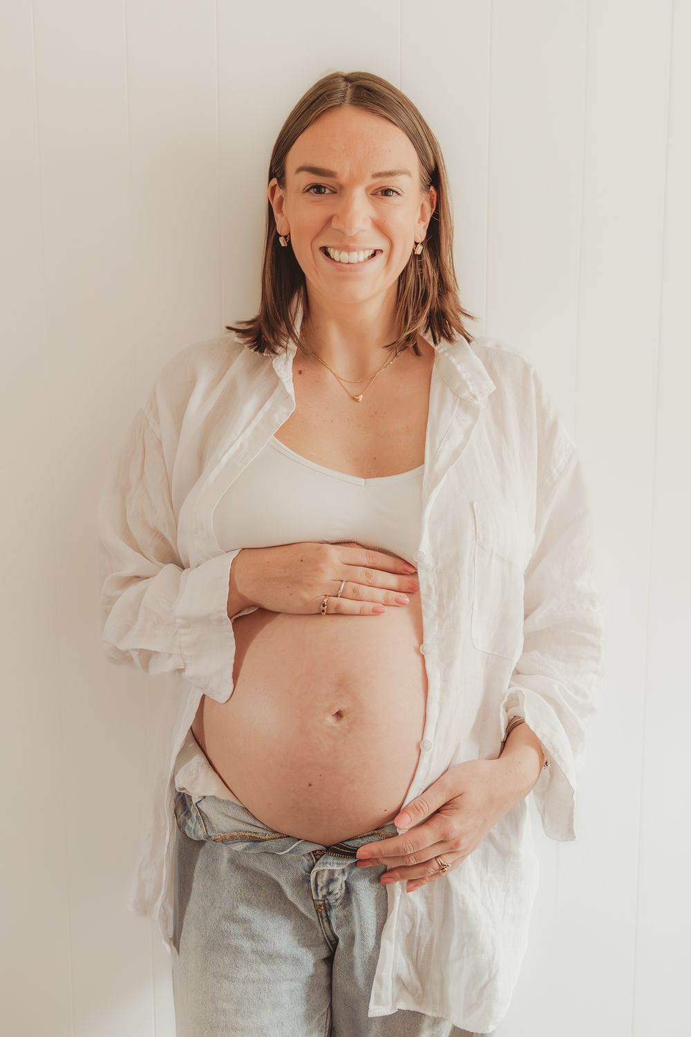 A pregnant person wearing a white button-down shirt shows the progression of their growing belly in four connected photos.