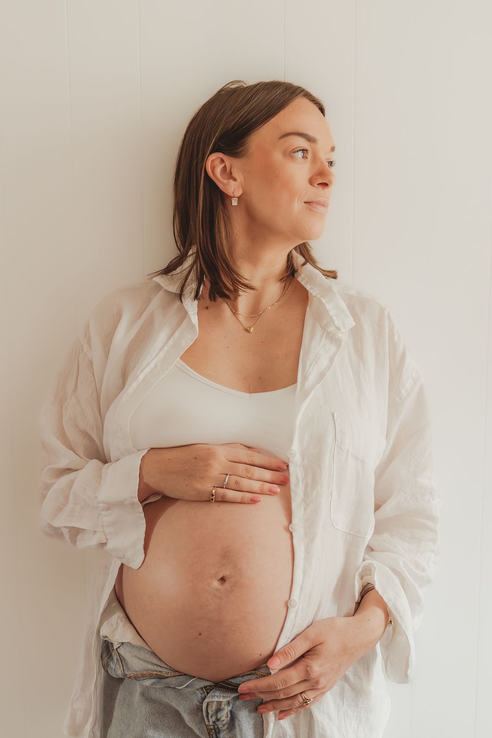 A series of pregnancy progression photos showing a growing baby bump against a white background in casual attire.