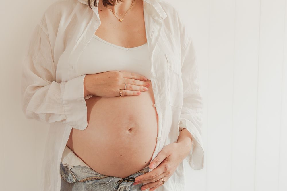 Pregnant woman in white sheer top holds her belly in a series of intimate maternity photos against white background.