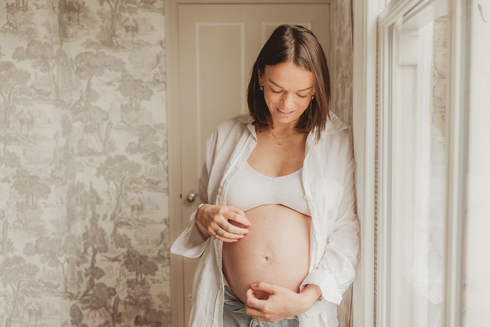 A person wearing a white cardigan holds and gazes lovingly at a newborn baby in a peaceful nursery setting.
