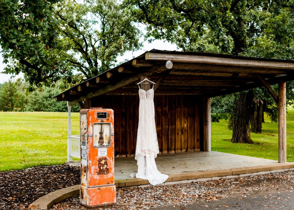 A white wedding dress hangs on display at a rustic wooden venue with vintage decor.