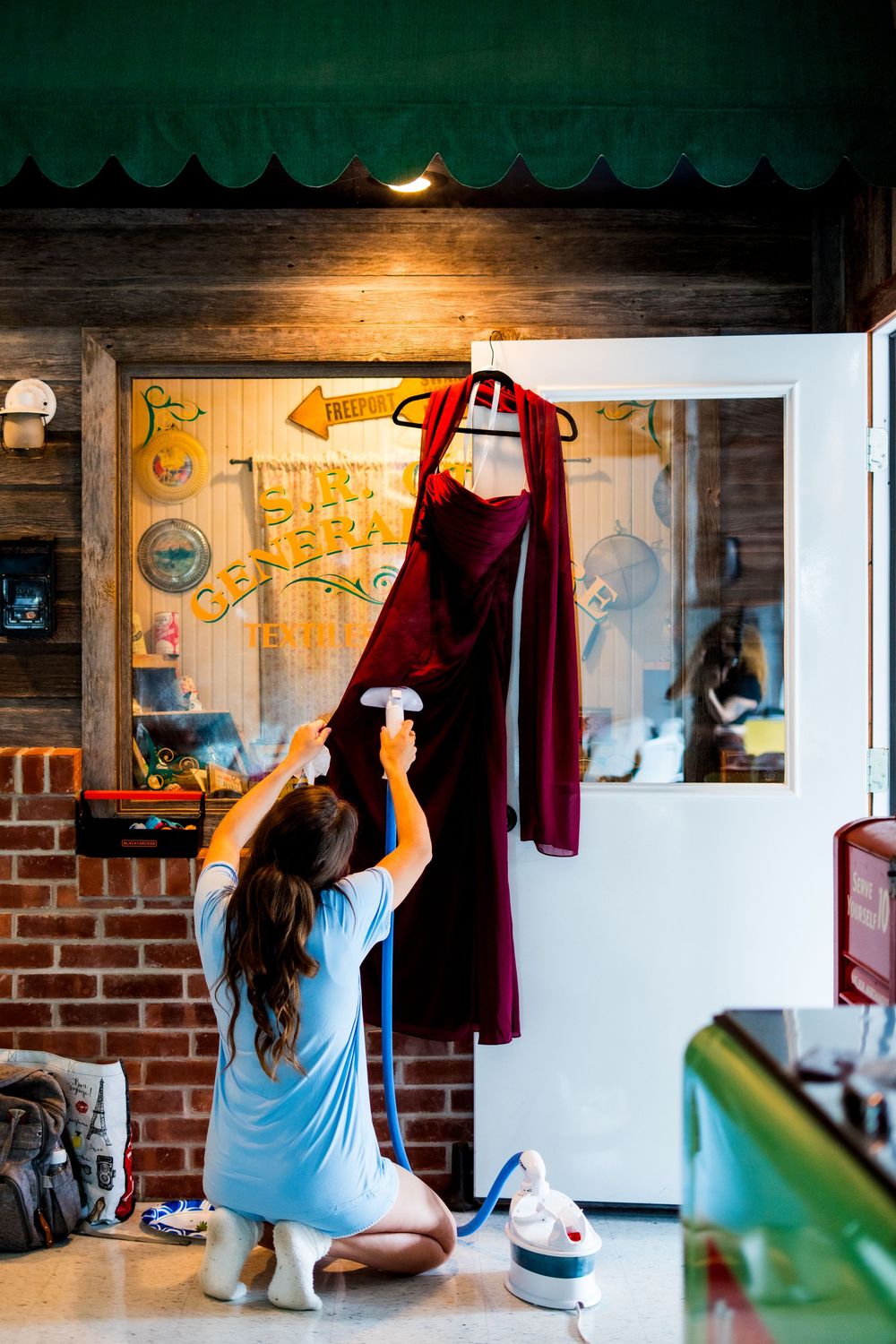 Someone in blue adjusts clothing on hangers in a rustic dressing room with wooden walls.