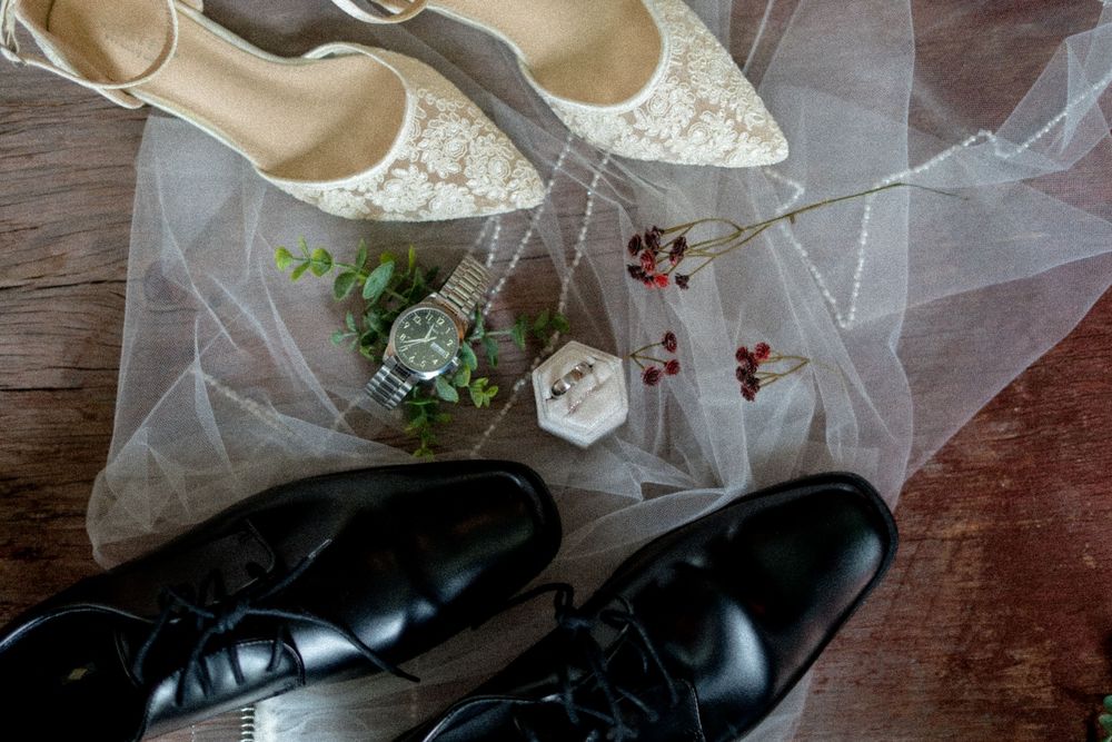 Wedding shoes arranged with delicate lace veil on wooden floor.