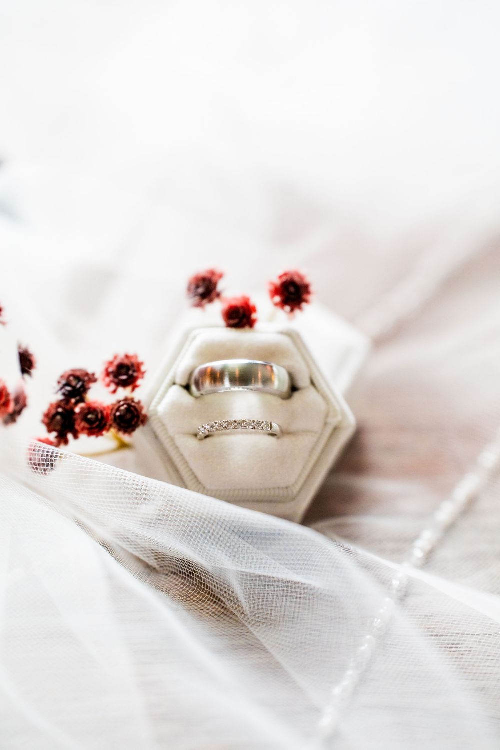Wedding rings displayed on white hexagonal holder with delicate red flowers.