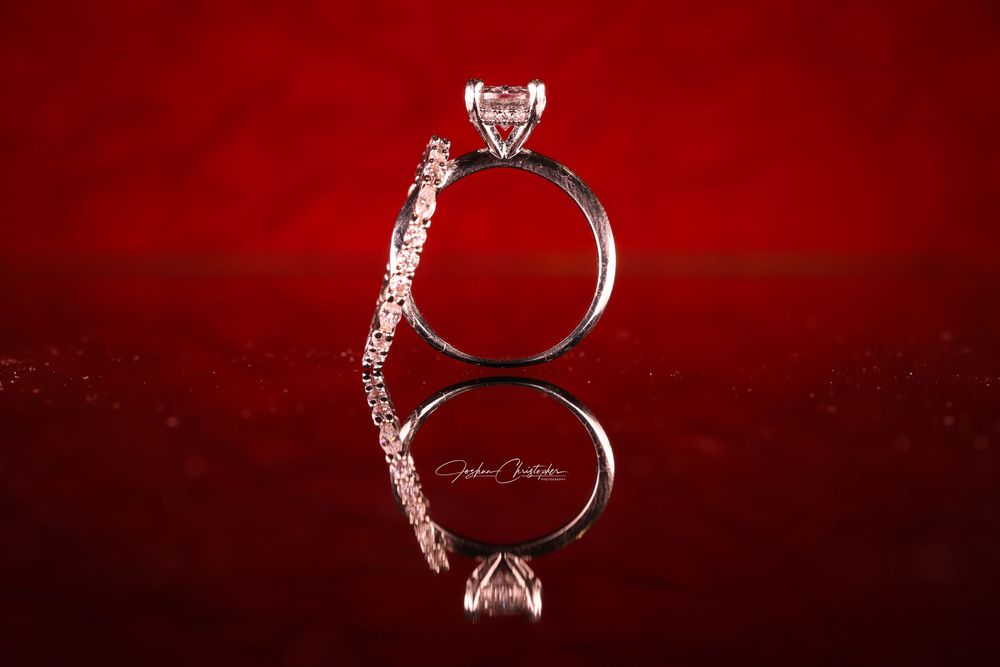 Elegant diamond engagement ring with reflection on red background showcasing intricate band details.