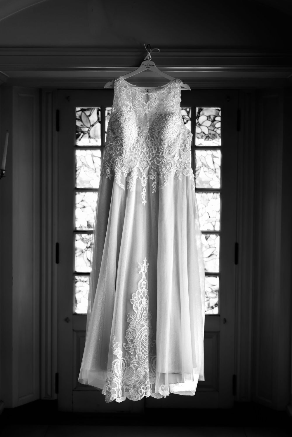 Elegant white wedding dress hanging in window light creating dramatic silhouette.