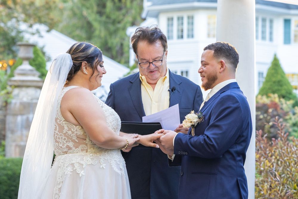 Wedding ceremony moment showing exchange of rings in outdoor garden setting.