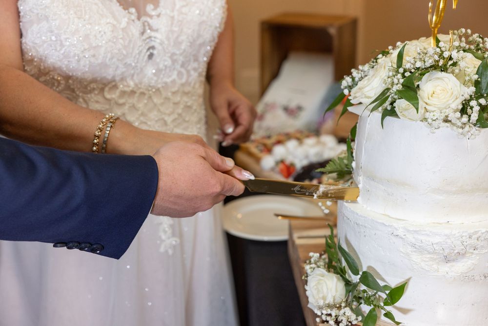 Close up of hands cutting into an elegant white tiered wedding cake.