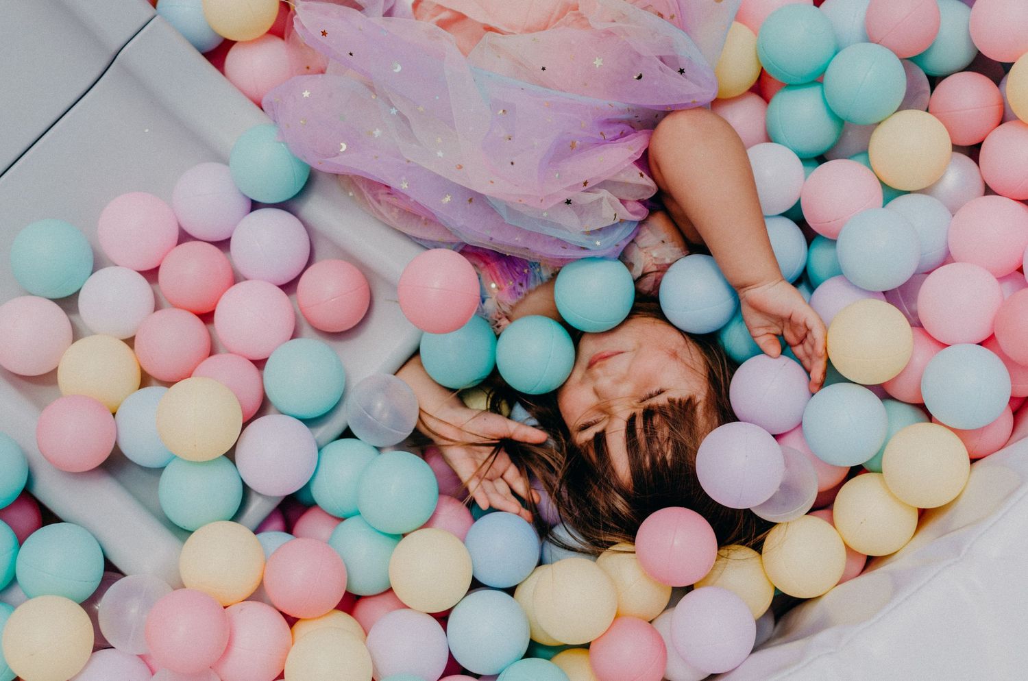 Person laying in a ball pit filled with pastel colored balls.