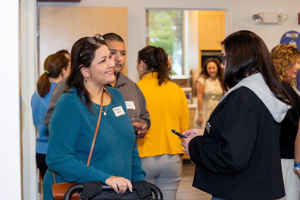 People gather and interact at a professional networking event in a bright indoor space.