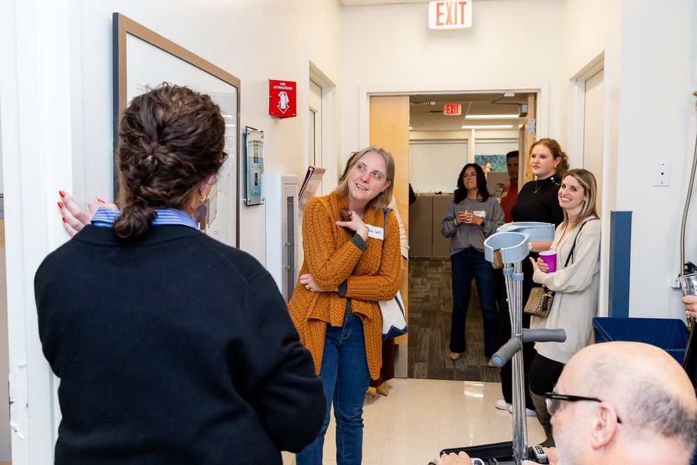 People gather in a bright hallway having animated conversations near an exit sign.