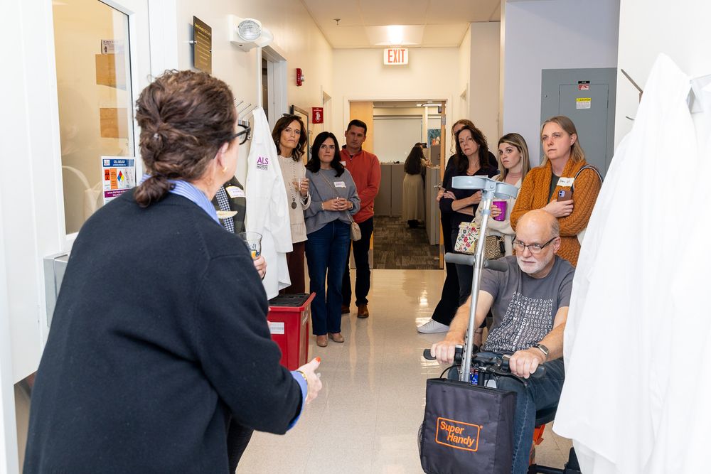 A group mingles and socializes in a bright white hallway during a business or networking event.
