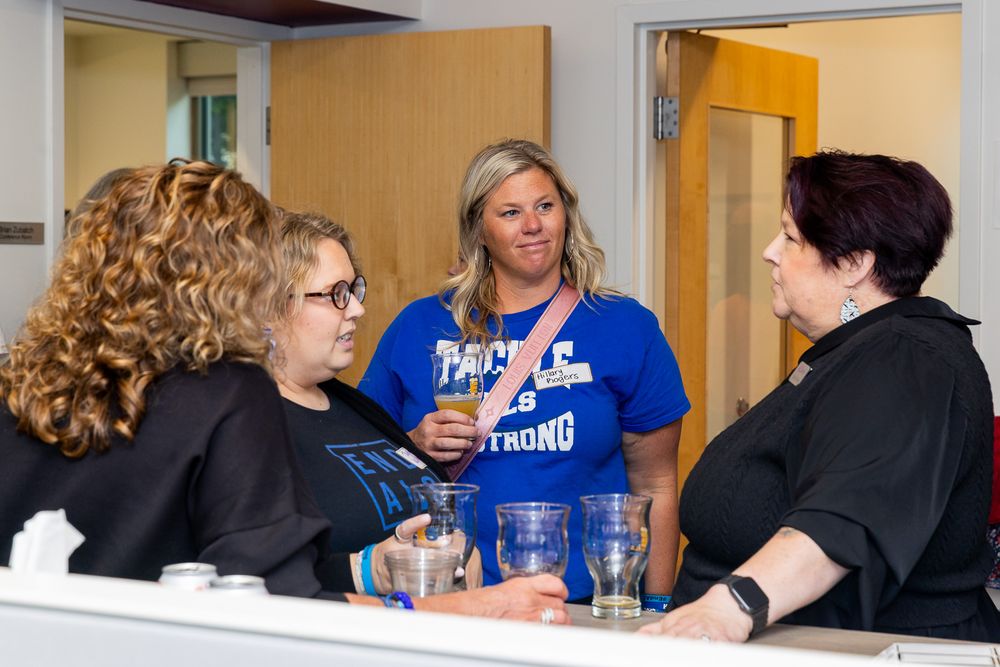 Three people having a conversation in an office setting, with two wearing black and one wearing a bright blue shirt.