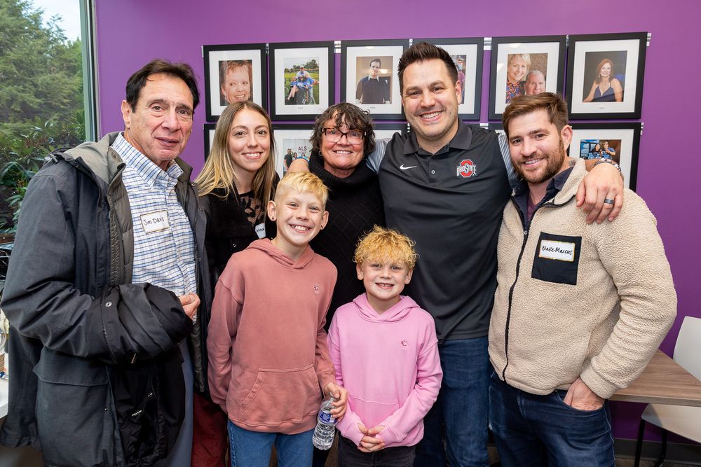 A group poses together for a photo against a purple wall with framed pictures in the background.
