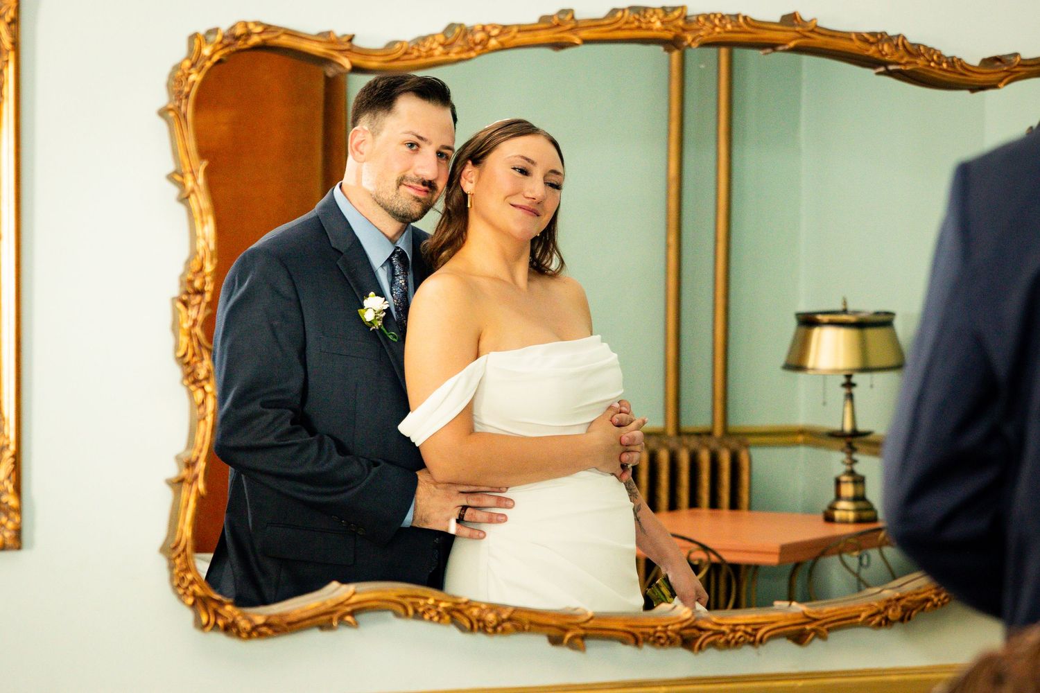 A bride and groom share an intimate moment together in front of an ornate gold mirror during their wedding celebration.
